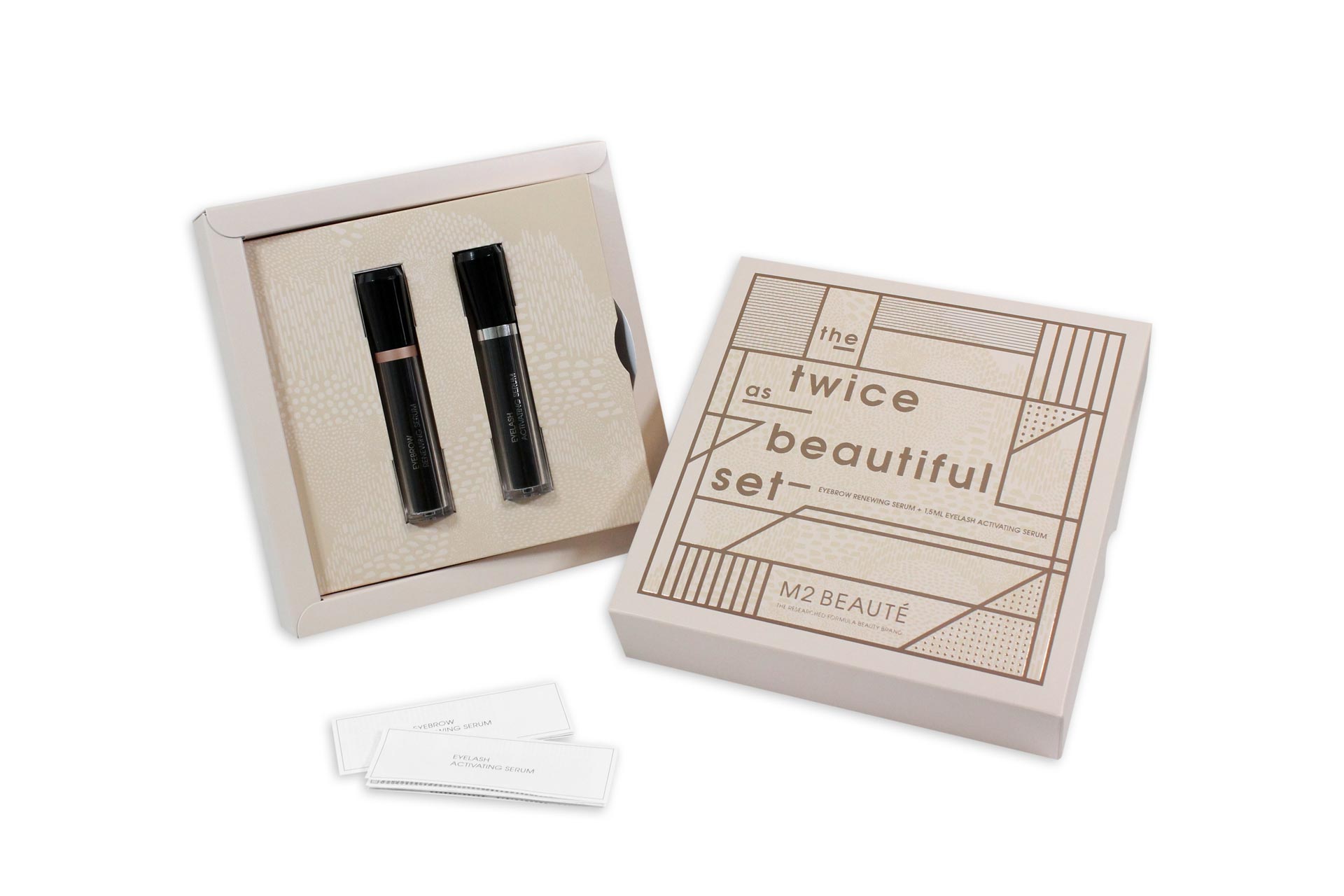 Cremefarben, geöffnete Präsentationsverpackung von M2 Beaute mit einem Inlay in dem zwei Beautyprodukte stecken. Davor liegen zwei kleine, zusammengefaltete Gebrauchsanweisungen. 