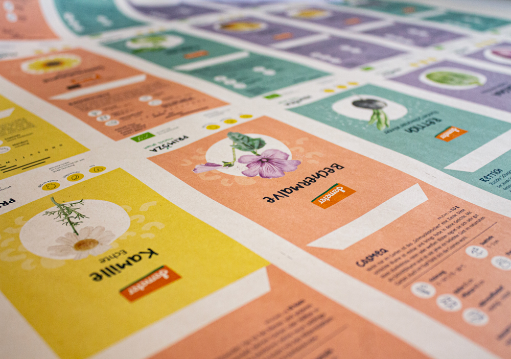 Ein flachliegender Druckbogen für Saatguttütchen mit unterschiedlichen Motiven in den Farben gelb, orange, türkis und lila