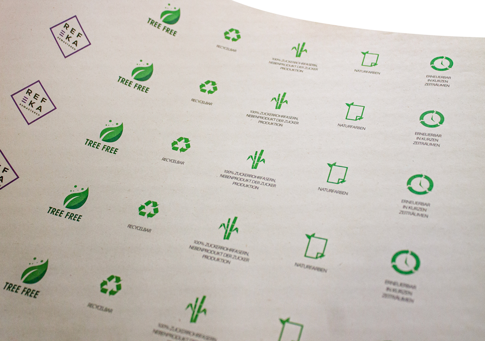 Ein flach daliegender Druckbogen mit grünen Icons und dem lila REFEKA Logo